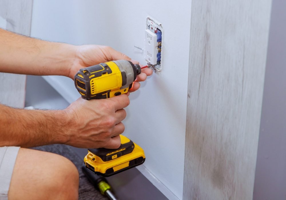 When constructing a house, electrician uses a screwdriver to install an outlet on wall